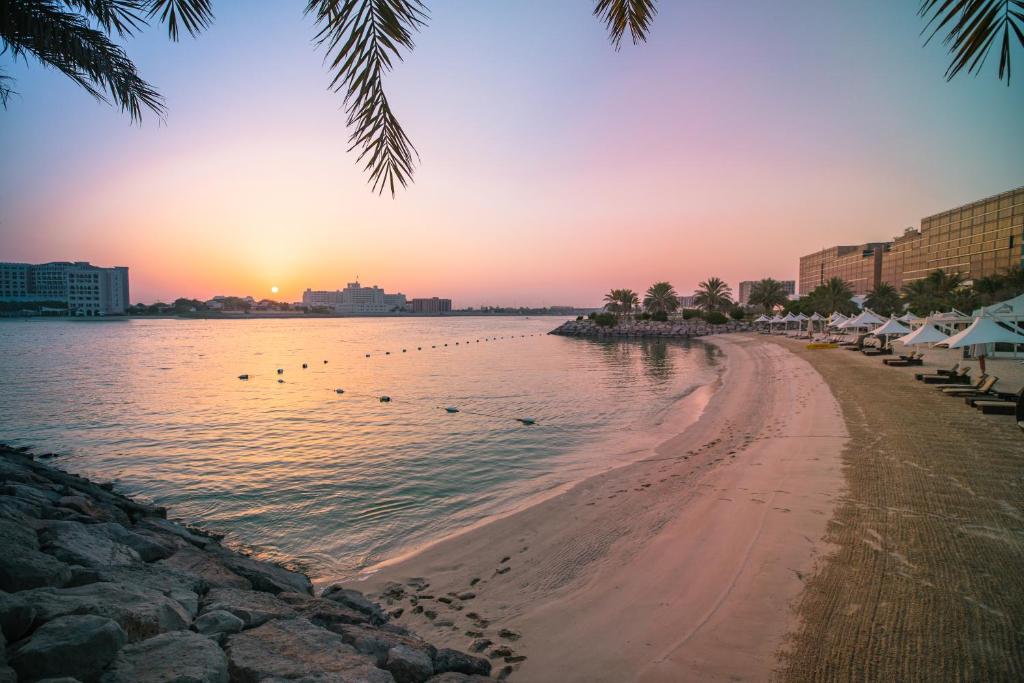 a beach at sunset with the sun setting over the water at Traders Hotel, Abu Dhabi in Abu Dhabi