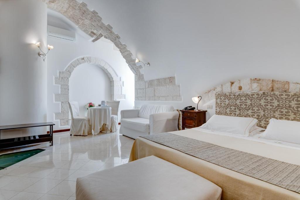 オストゥーニにあるホテル ラ テラのベッド2台とソファが備わる広い白い客室です。