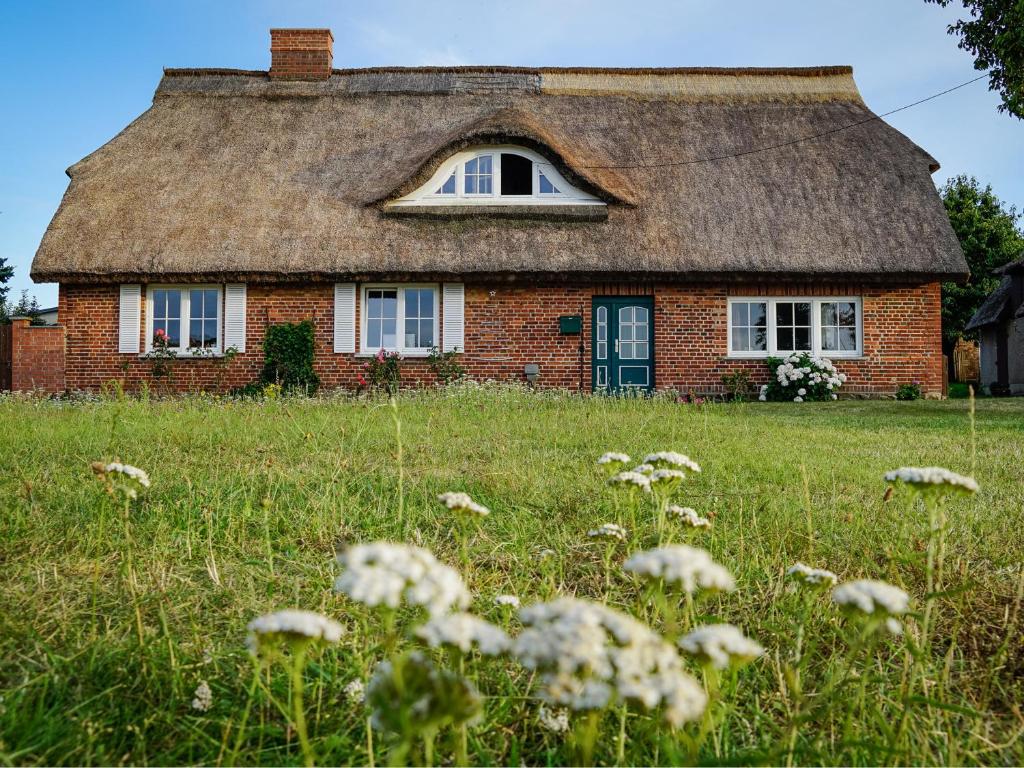 an old brick house with a thatched roof in a field at Ferienhaus Gut Glück in Lancken-Granitz