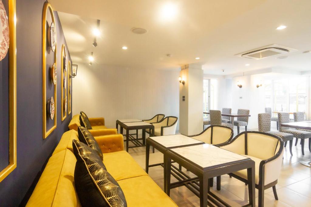 a waiting room with a yellow couch and tables and chairs at Montree Phuket Hotel in Phuket Town