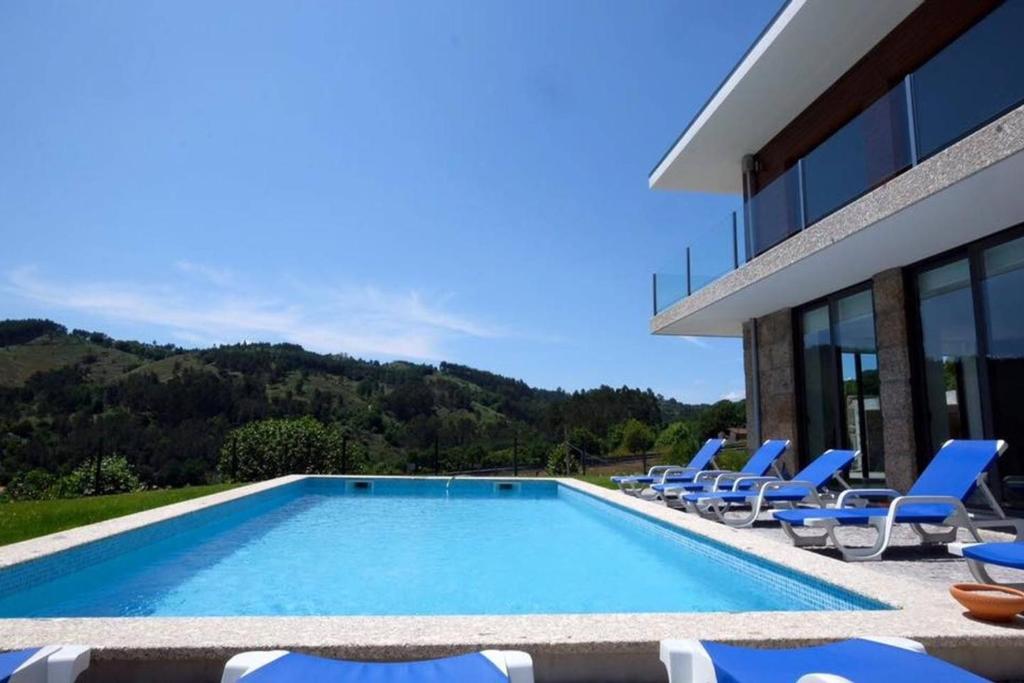 uma piscina com cadeiras e um edifício em 5 bedrooms villa with private pool furnished garden and wifi at Vieira do Minho em Vieira do Minho