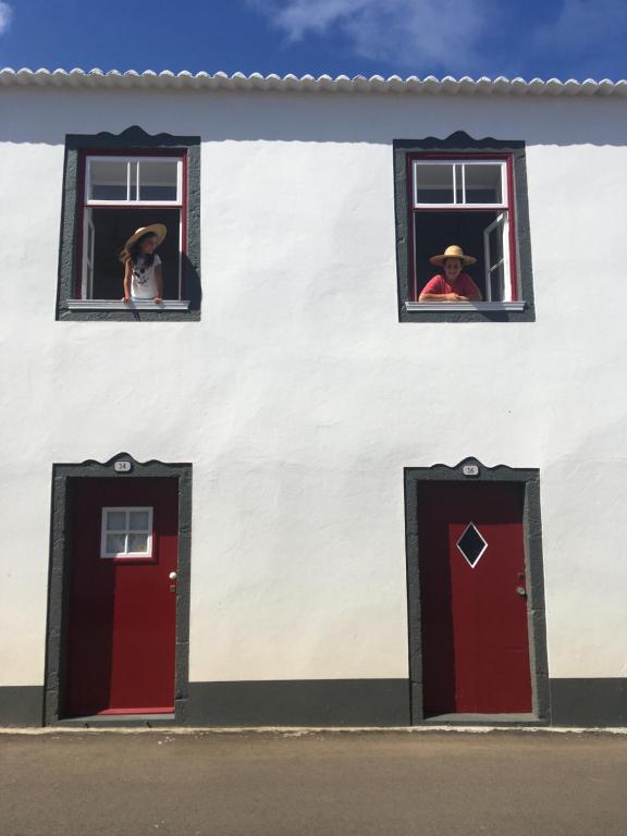 two people in the windows of a white building with red doors at Graciosa Family House in Santa Cruz da Graciosa