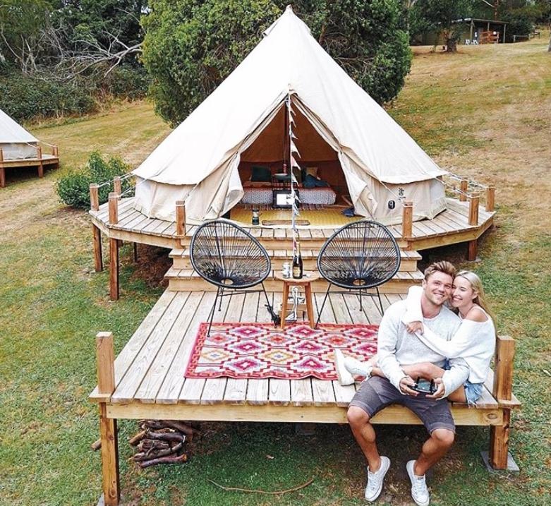 un homme et une femme assis sur un banc en bois devant une tente dans l'établissement Iluka Retreat Glamping Village, à Red Hill South