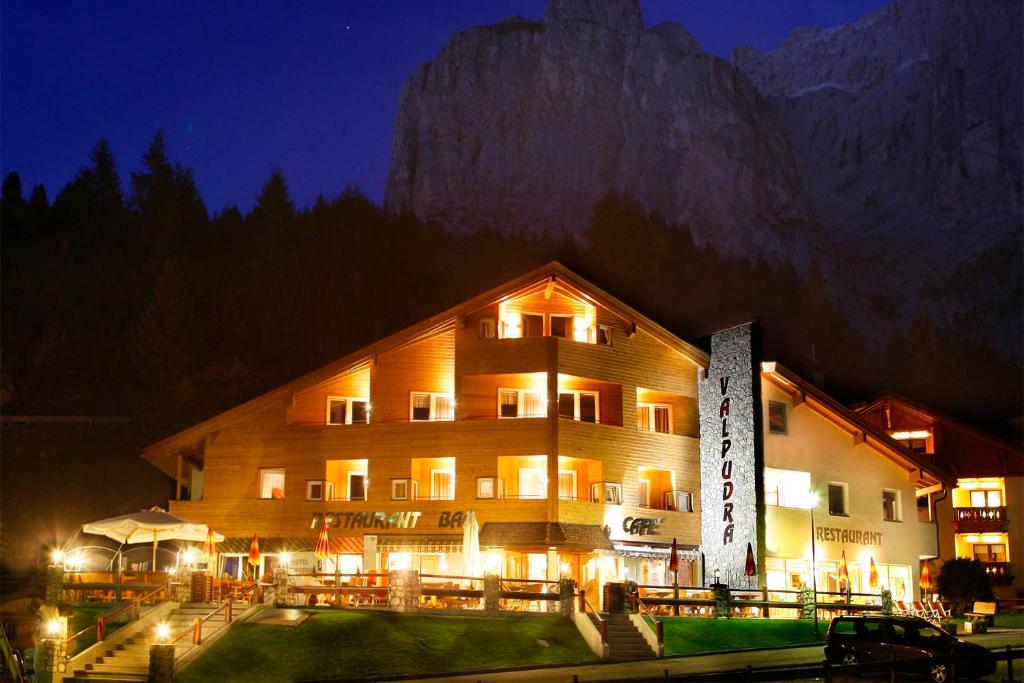 un grand bâtiment avec une montagne derrière lui la nuit dans l'établissement Hotel Valpudra, à Selva di Val Gardena