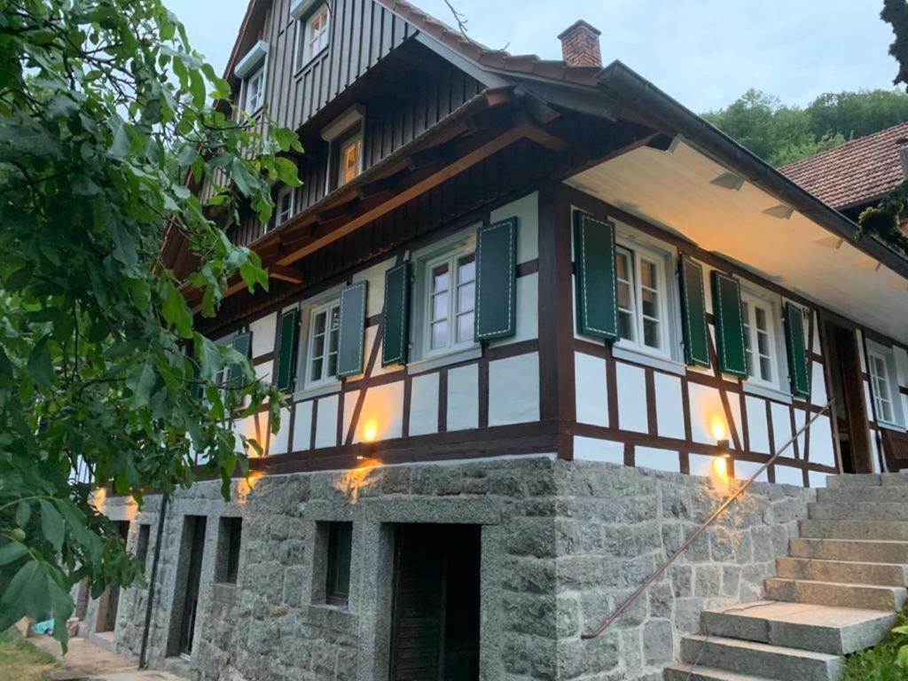 a house with green shuttered windows and a stone wall at Huber Xaveri - Hof in Ottenhöfen