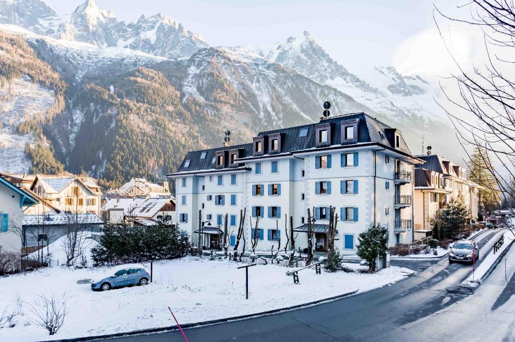 a large white building on a snowy street with mountains at Le Paradis 25 Apartment - Chamonix All Year in Chamonix