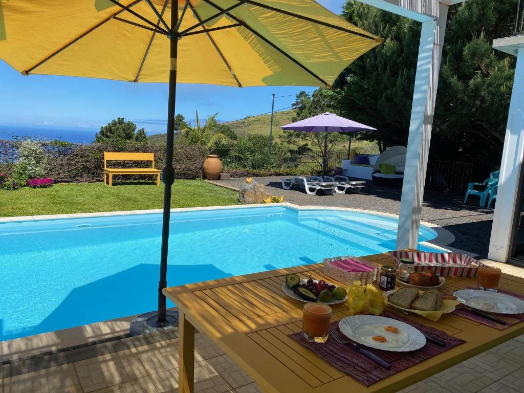 uma mesa com comida e um guarda-sol junto a uma piscina em Casa de Prazeres em Prazeres