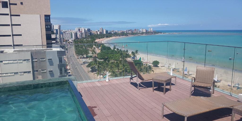 un balcón con sillas, una piscina y una playa en Pajuçara Front Beach en Maceió