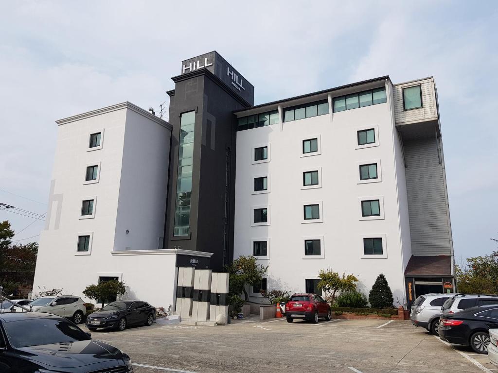 een wit gebouw met auto's geparkeerd op een parkeerplaats bij Goodstay Motel Hill in Gangneung