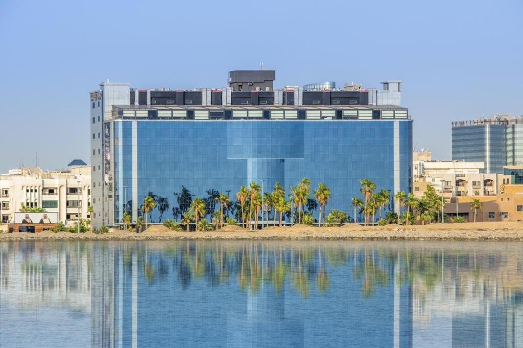 فندق ميرا الواجهة البحرية جدة  في جدة: مبنى يوجد به نخيل امام اجزاء من الماء