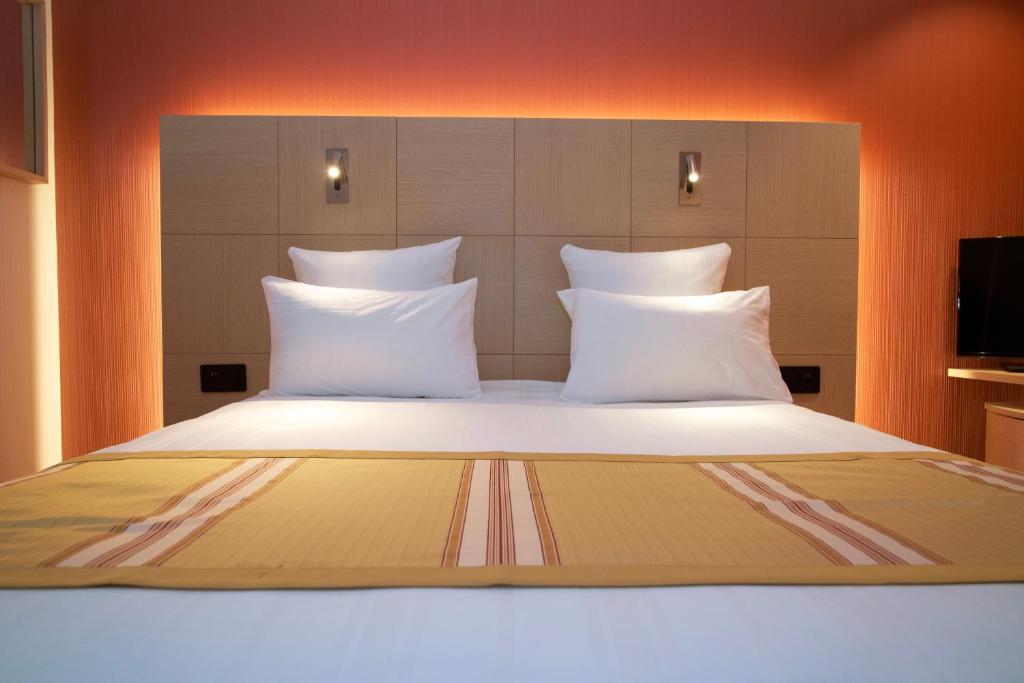 a large bed with white pillows in a room at Nash Airport Hotel in Geneva
