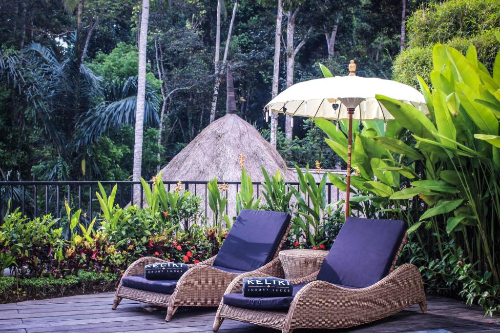 two chairs and an umbrella on a deck at Keliki Luxury Lodge in Ubud