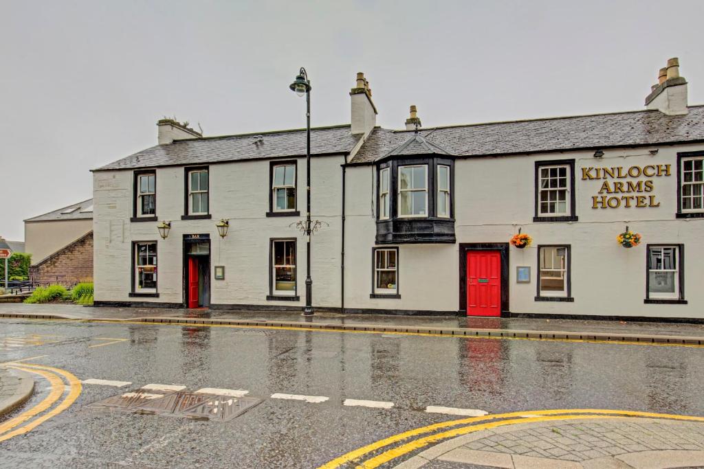 een wit gebouw met rode deuren in een regenachtige straat bij Kinloch Arms Hotel in Carnoustie