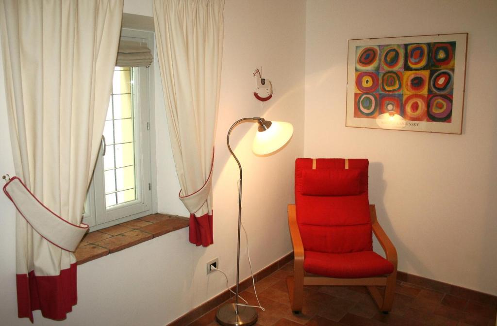 Cette chambre dispose d'une chaise rouge, d'une lampe et d'une fenêtre. dans l'établissement Appartamenti Urbevetus, à Orvieto