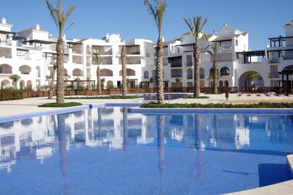 una piscina frente a un edificio con palmeras en Apartamento en la Torre Golf Resort, en Torre-Pacheco