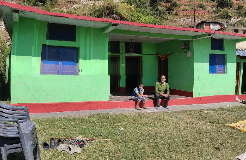 un homme et une femme assis à l'extérieur d'une maison verte dans l'établissement Solitude Homestay, Agoda, à Uttarkāshi