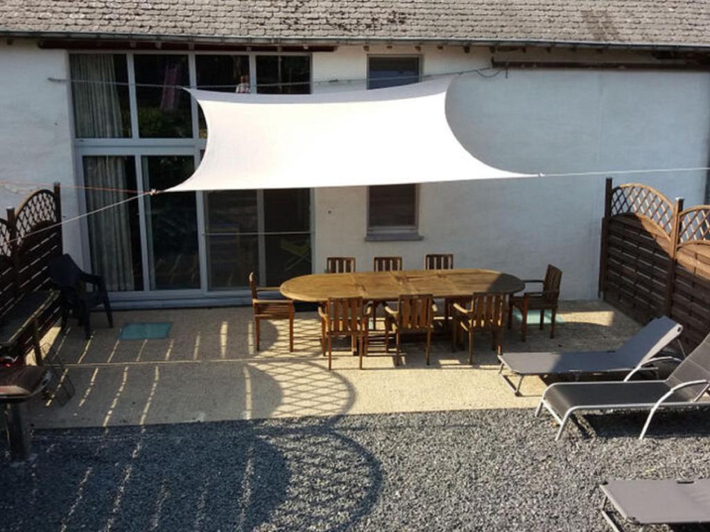 un patio con mesa, sillas y una sombrilla blanca en Rural lodging located in the small village of Radelange 100 Nature en Radelange