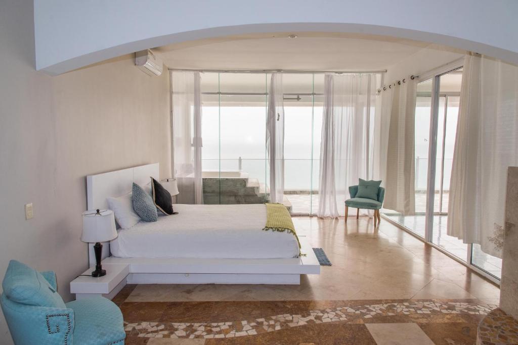 a white bedroom with a bed and a chair at Oceanfront Serenity in Gated Community near Rosarito in Harry Manzo