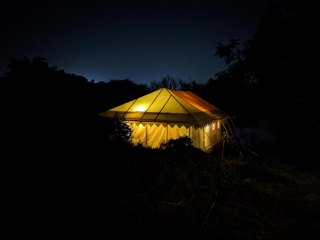 une tente éclairée dans l'obscurité la nuit dans l'établissement Dera Baghdarrah Nature Retreat Udaipur, à Udaipur