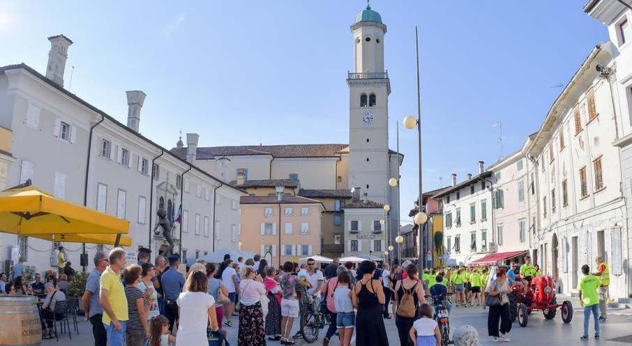 tłum ludzi idących ulicą z wieżą zegarową w obiekcie Friuli Appartamenti w mieście Cormòns