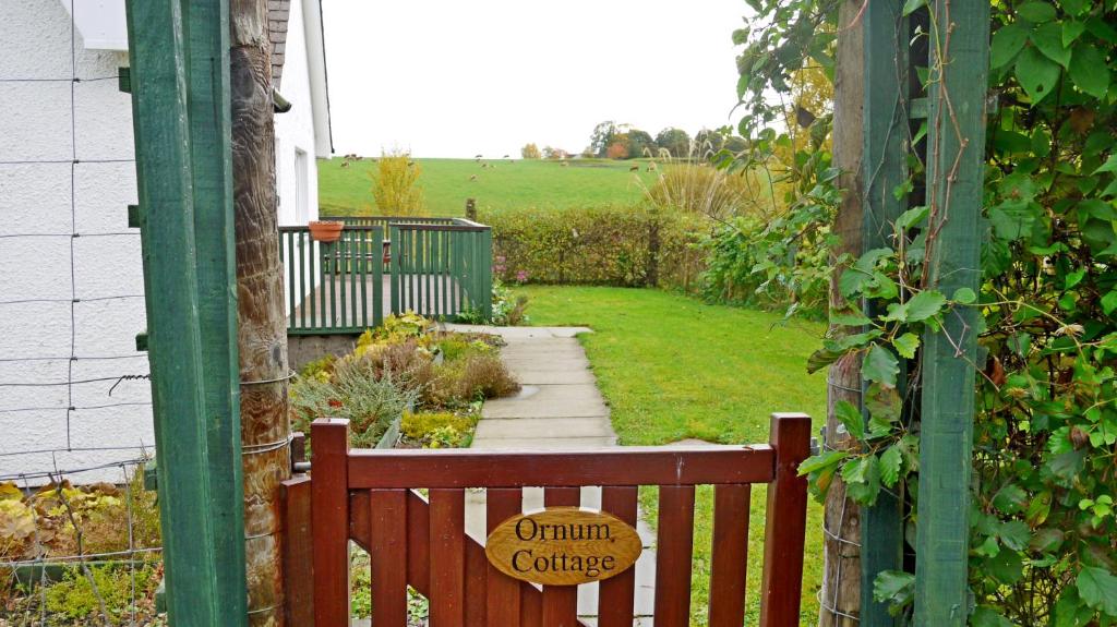 un banco de madera en un jardín con un cartel en Ornum Cottage, en Beauly