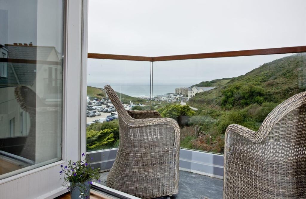 two wicker chairs sitting on a balcony looking out at the ocean at 10 The Whitehouse, Watergate Bay in Porth