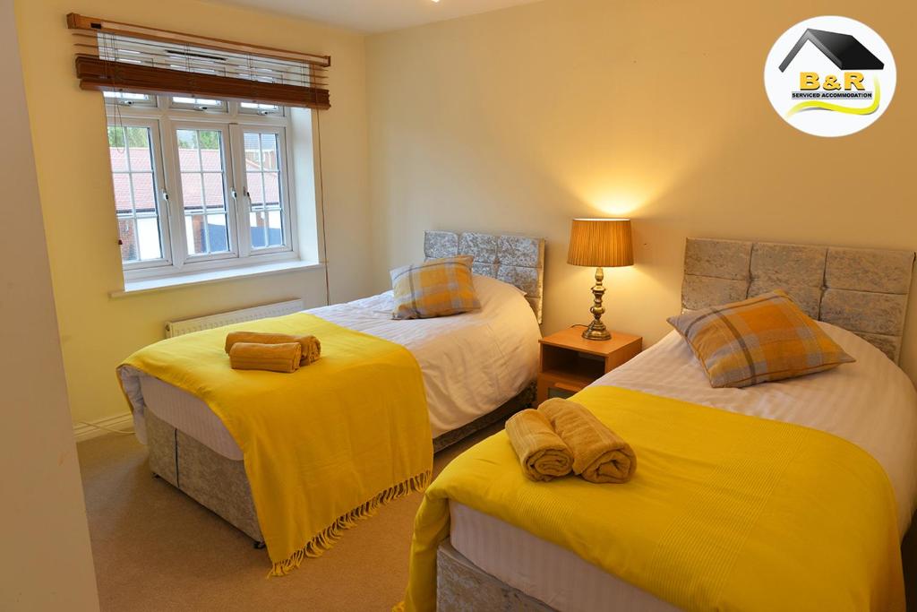 - une chambre avec 2 lits avec des draps jaunes et une fenêtre dans l'établissement B and R Serviced Accommodation Amesbury, 3 Bedroom House with Free Parking, Super Fast Wi-Fi 145Mbs and 4K smart TV, Archer House, à Amesbury