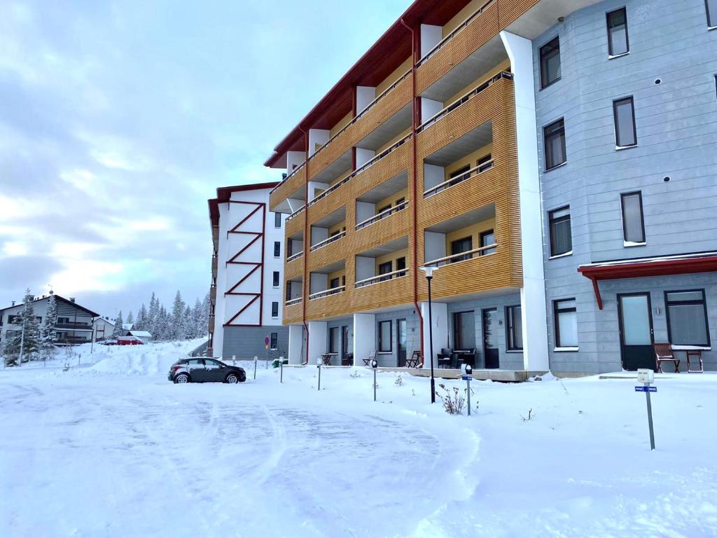 Enjoy Ylläs - Cozy top floor apartment في يلاسشارفيه: موقف سيارات مغطى بالثلج أمام مبنى