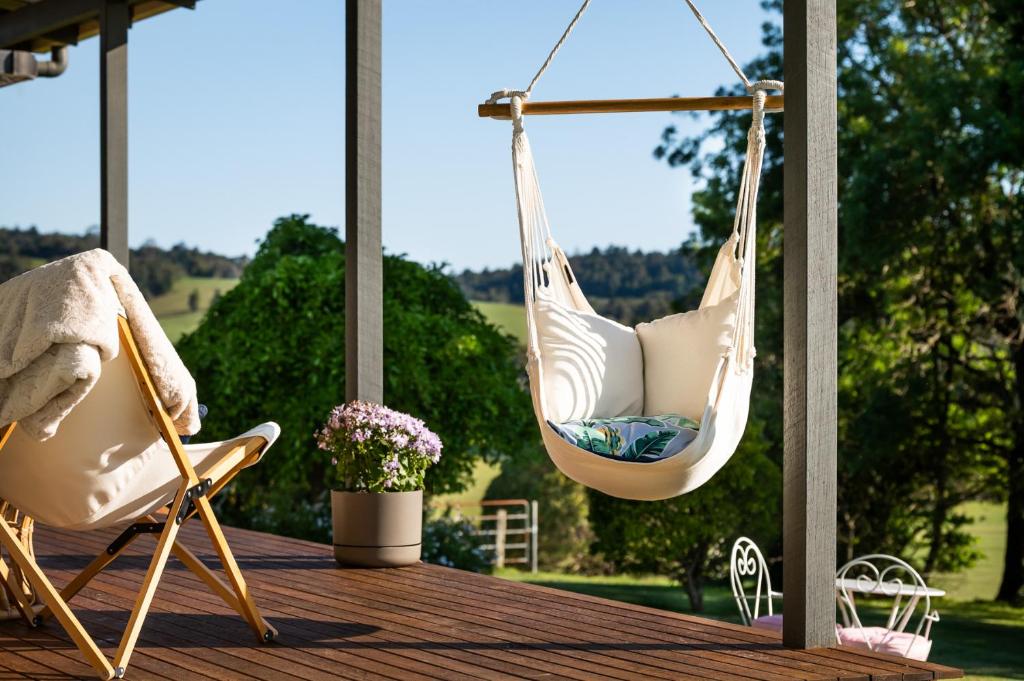 a porch with two swings and two chairs on a deck at Fay's Cottage in Dorrigo