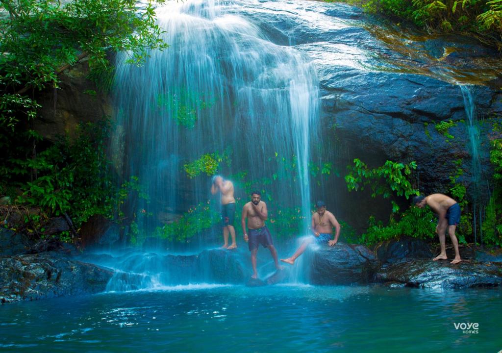 un groupe d'hommes debout dans l'eau près d'une cascade dans l'établissement Moonlight Munnar Forest Bungalow with Private Waterfalls by VOYE HOMES, à Kanthalloor