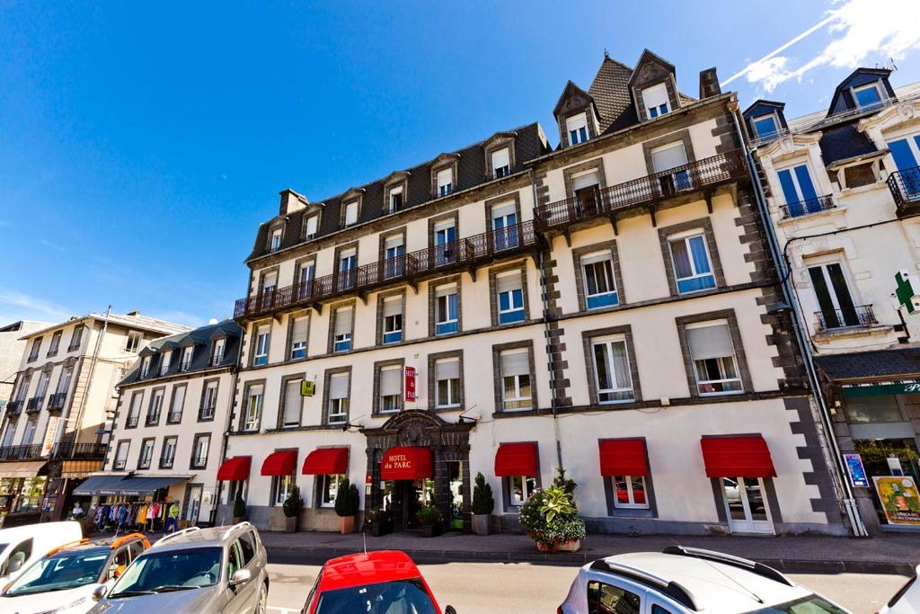 a large building with cars parked in front of it at Hôtel du Parc in Le Mont-Dore