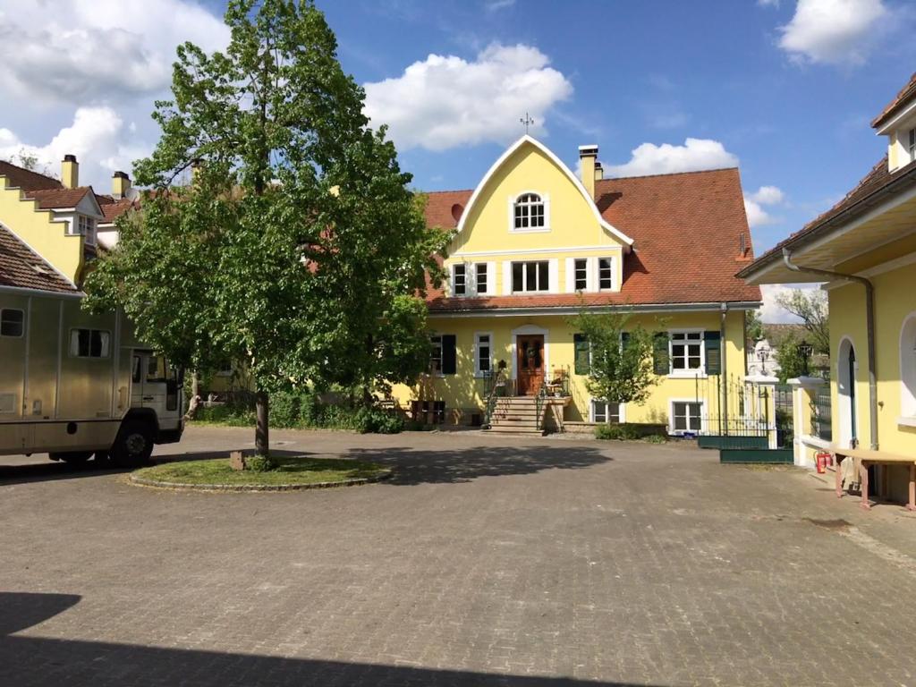 a yellow house with a tree in a parking lot at Ferienwohnung im Grünen auf idyllisch gelegenen Gutshof und doch so zentral in Waldshut-Tiengen