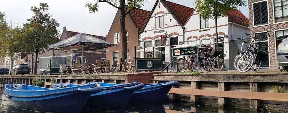 エダムにあるHotel - Cafe De Harmonieの水上に建つ建物の隣に座る青い船2隻