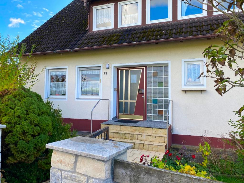 une maison blanche avec une porte rouge et quelques fleurs dans l'établissement Ferienwohnungen / Ferienhaus Dillingen an der Donau, à Dillingen an der Donau