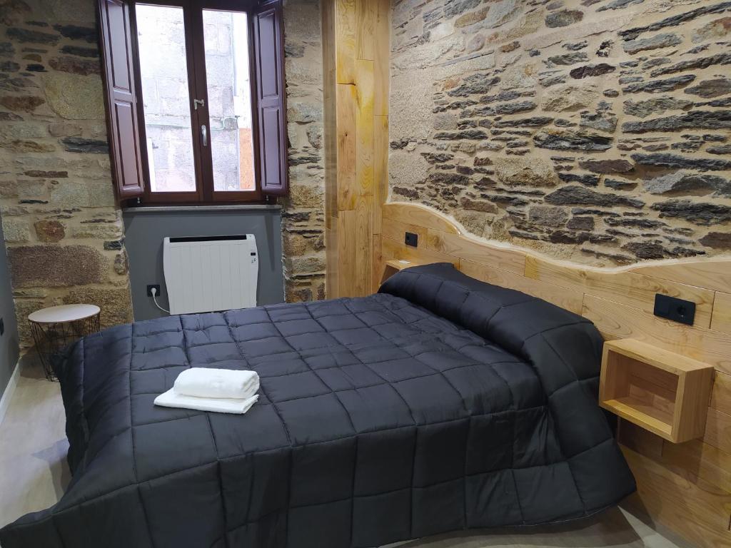 a bedroom with a black bed in a stone wall at Apartamentos turísticos o palomar in Villalba