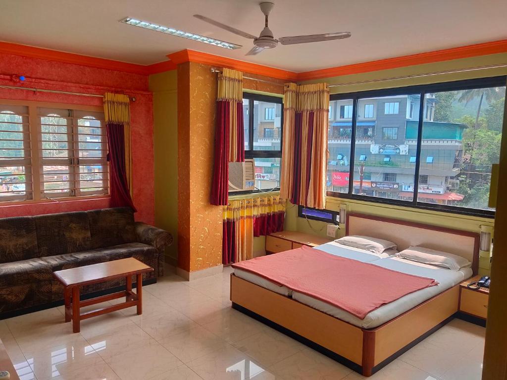 a bedroom with a bed and a couch and windows at Hotel Ayodhya in Chiplun