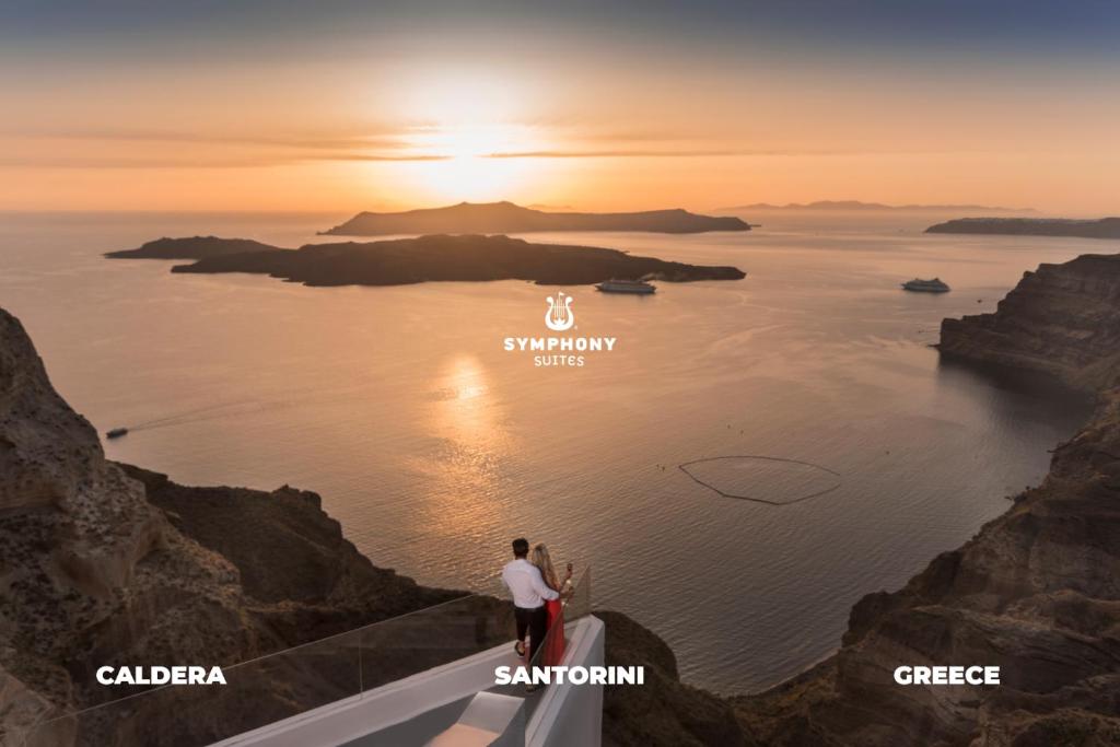 a couple standing on the edge of a cliff looking at the ocean at Symphony Suites Santorini in Pirgos