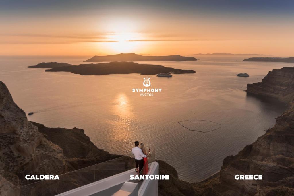 a couple standing on the edge of a cliff looking at the ocean at Symphony Suites Santorini in Pyrgos