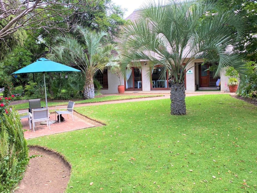 a garden with two chairs and a table and an umbrella at Safari Club Guest Lodge OR Tambo International Airport in Kempton Park