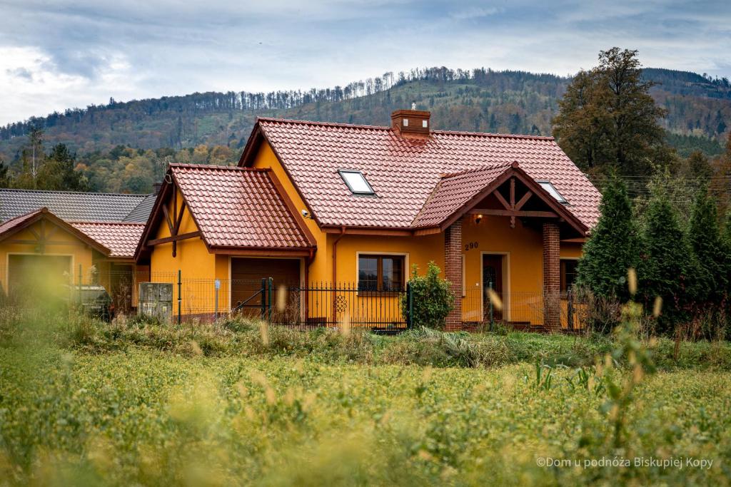 ein gelbes Haus mit braunen Dächern auf einem Feld in der Unterkunft Dom u podnóża Biskupiej Kopy in Jarnołtówek