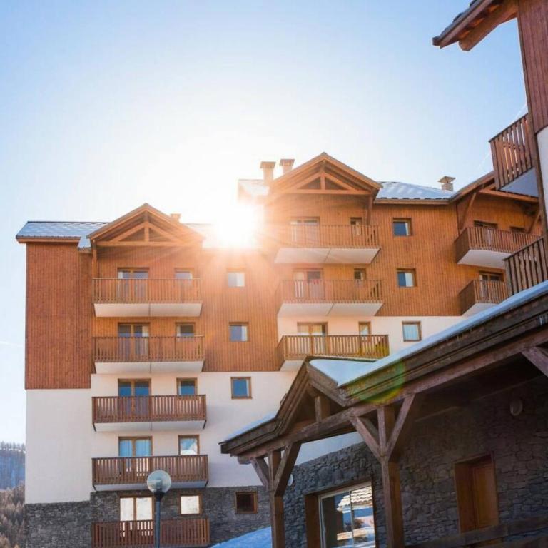 un grand bâtiment avec un coucher de soleil derrière dans l'établissement Residence Les Gentianes - maeva Home, à Puy-Saint-Vincent
