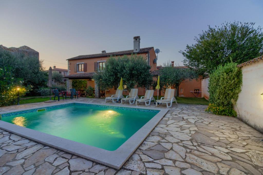 a swimming pool in a yard with chairs and a house at Beautiful stone istrian villa Anamaria with pool near the beach in Šišan
