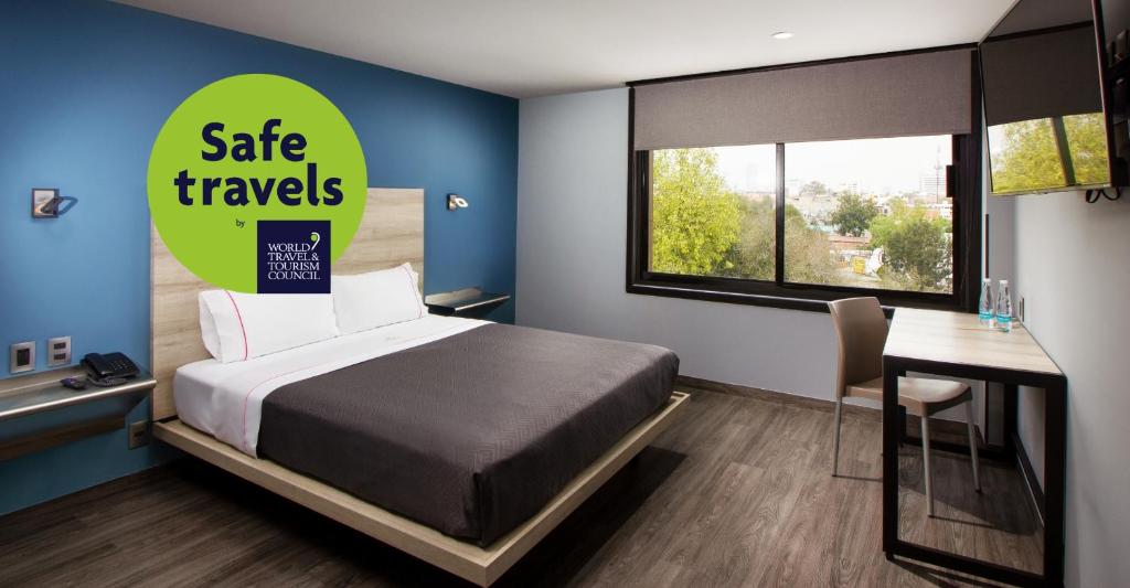 A guest room with one bed, a desk, open wardrobe, and a broad city-facing window.