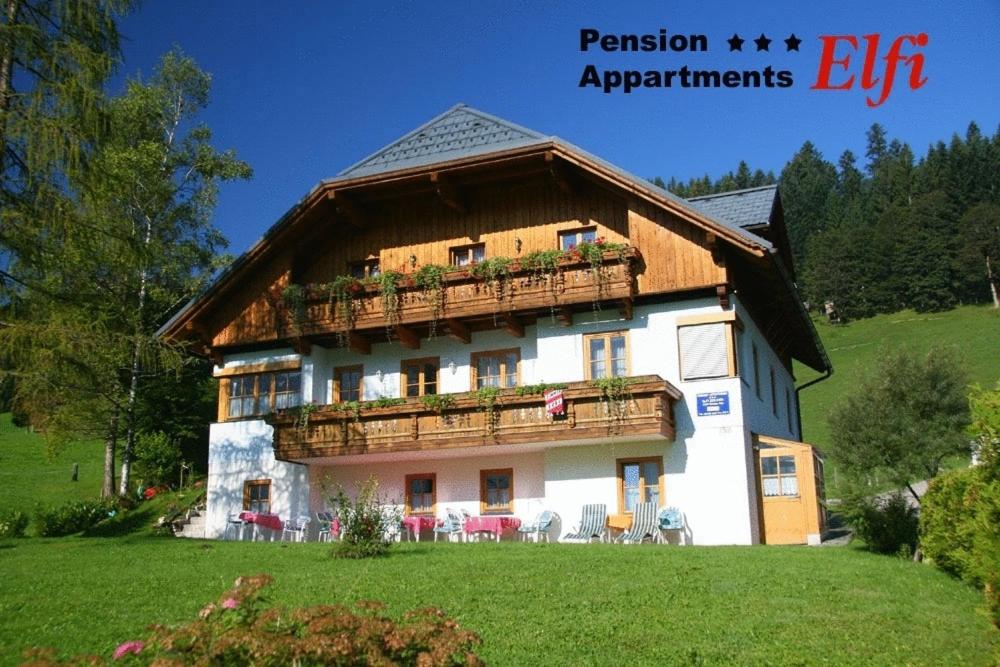 a large house with a balcony on a green field at Appartements Pension Elfi in Gosau