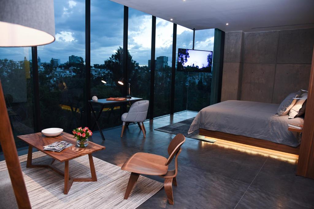 a bedroom with a bed and a table and a room with windows at Suites BQ in Guadalajara