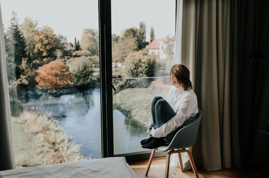 una mujer sentada en una silla mirando por una ventana en Sternen Bohlingen Aparthotel en Singen
