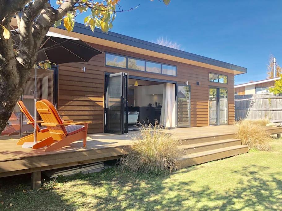 a house with a deck with a chair and an umbrella at Modern Kowhai Cottage in Wanaka