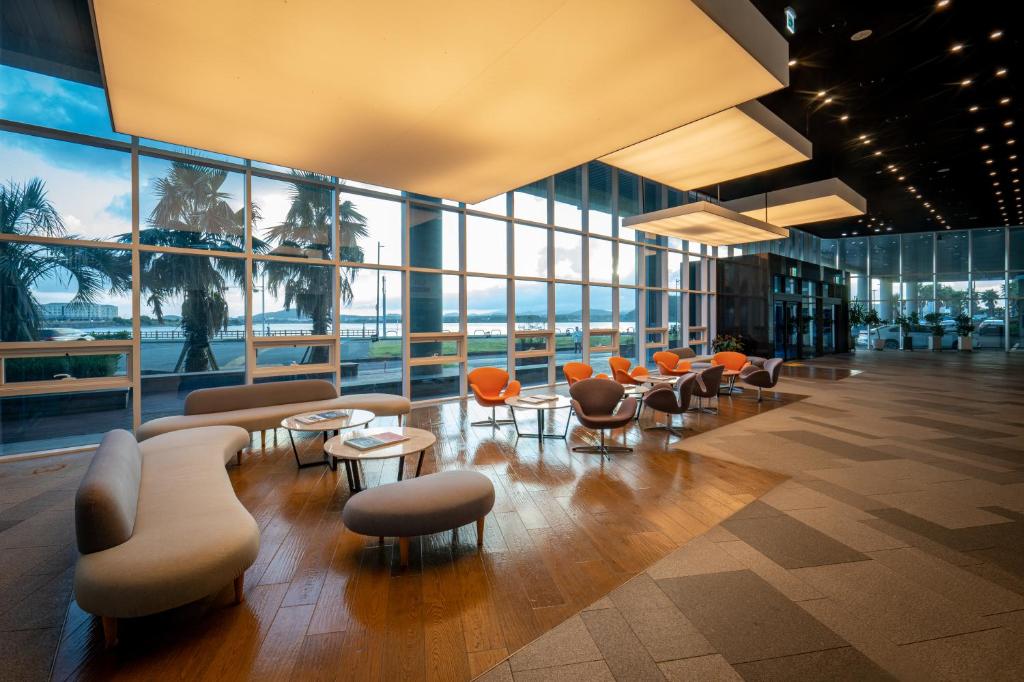 a lobby with orange chairs and tables and windows at Co-op City Hotel Seongsan in Seogwipo