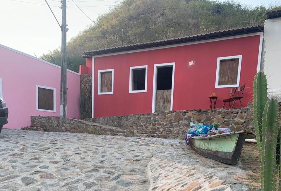 a red house with a boat in front of it at Casa Canoa - climatizada e com piscina in Piranhas