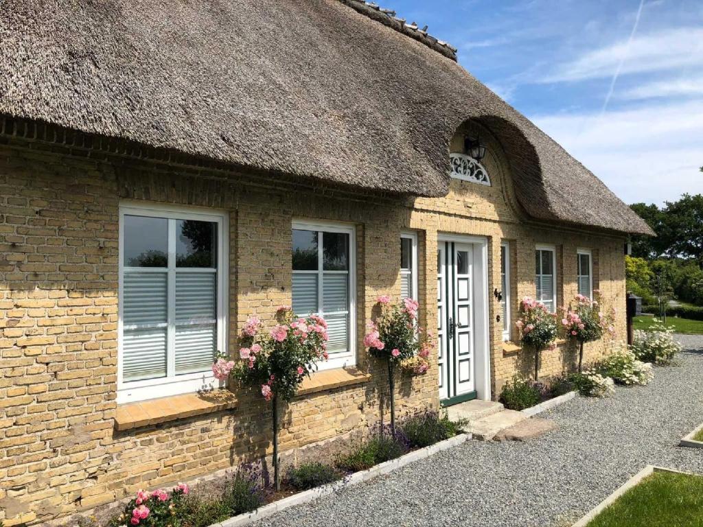 a house with a thatched roof with flowers in front at Reethaus Gaarwang in Gelting